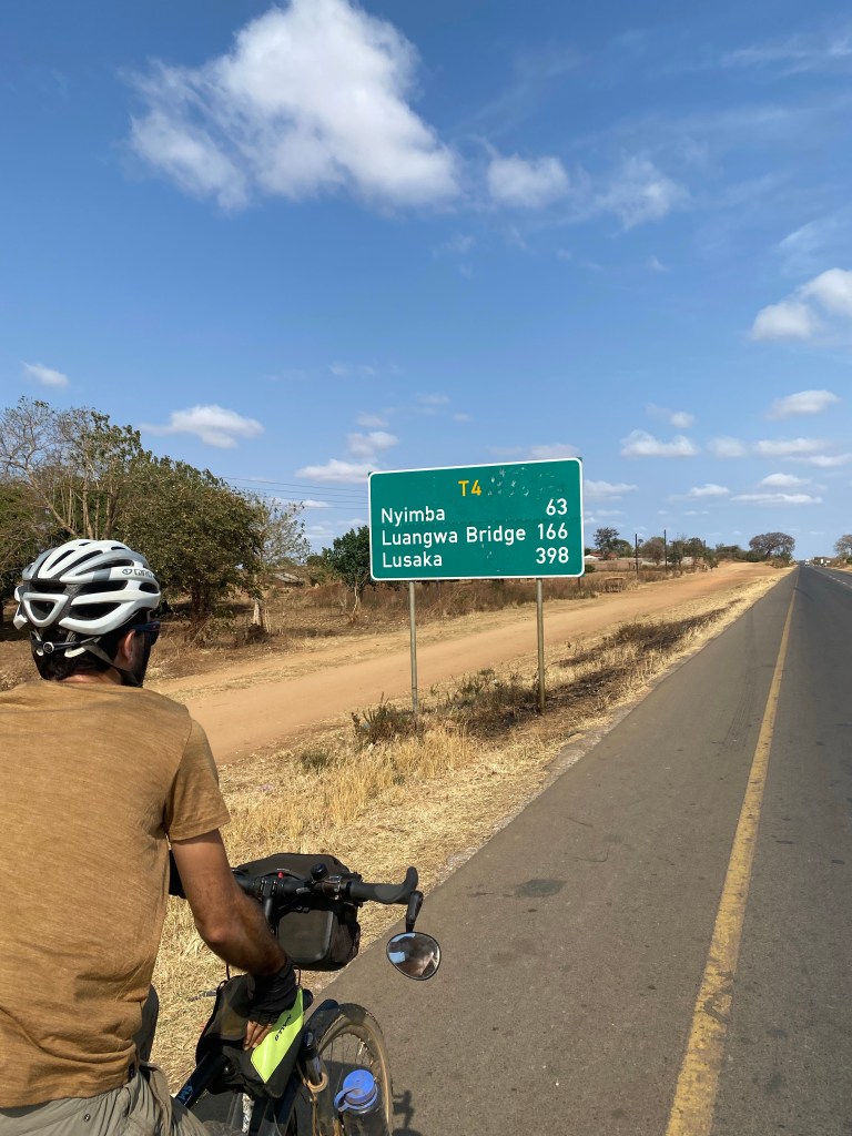 Javi biking next to the road sign showing Lusaka 