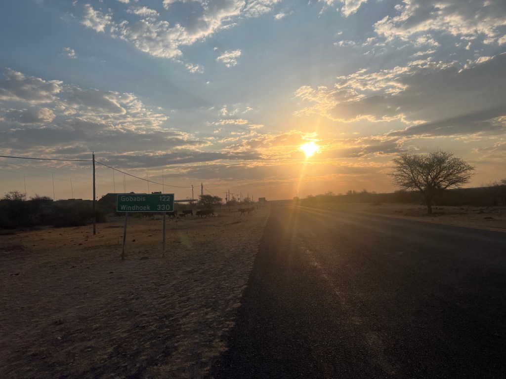 Sunset on a road in Botswana with a sign indicating Windhoek 