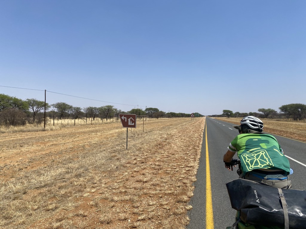 A cyclist in Namibia with a road sign showing a place to eat 